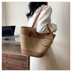 Macro detail of large straw tote bag featuring brown woven stripes and leather shoulder straps