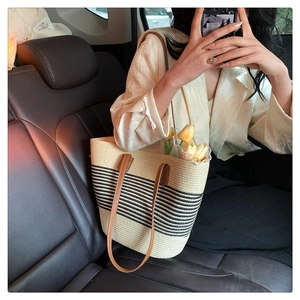 Detail of straw tote bag with black stripes and brown leather handles in a car