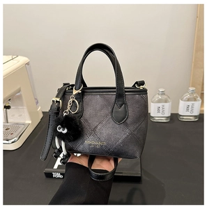 Detail of minimalist bucket bag with plaid texture, leather trim and plush pendant