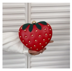 Detail of red strawberry-shaped clutch bag with golden rivet seeds and green leaf trim