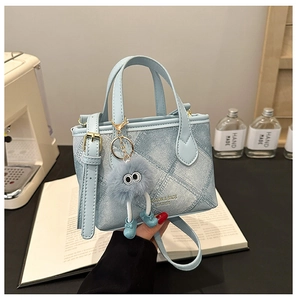 Detail of light blue bucket bag with denim texture and cute plush ball charm accessory