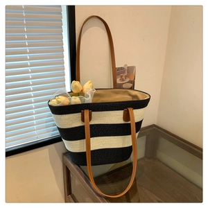 Detail of black and white striped straw tote bag with brown leather shoulder straps