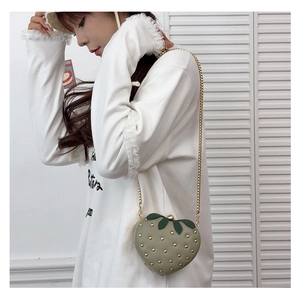 Model wearing strawberry shaped crossbody bag with gold rivets and metallic chain strap