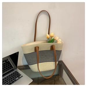 Detail of straw tote bag with black stripes and brown leather shoulder straps