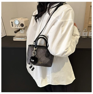 Detail of dark grey quilted bucket bag with black handle and decorative fur ball charm