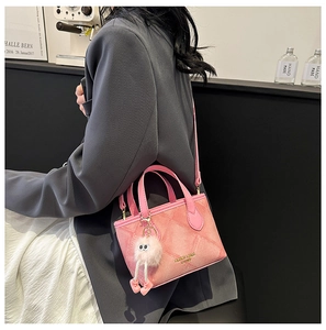 Detail of pink quilted bucket bag with plush charm on a crossbody strap worn by a model