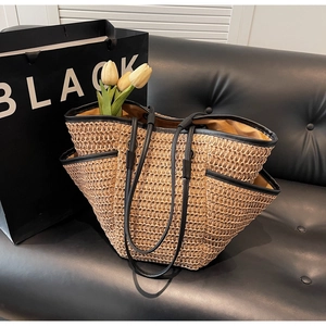 Détail du grand sac cabas en paille tissée avec bordure en cuir noir sur un canapé