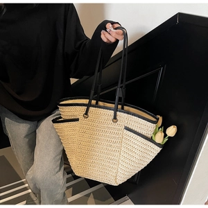 Détail du sac cabas en paille avec bordure et anses en cuir noir porté par un modèle