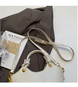 Close-up of a white glossy leather bucket bag with knot handles and gold hardware accents