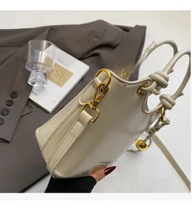 Detail of cream bucket bag featuring polished gold hardware and knotted handle design