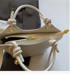 Close-up of a cream white bucket bag with a smooth metal zipper and knot handle detail