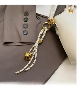 Detail of woven rope charm with golden bell and logo bead on bucket handbag