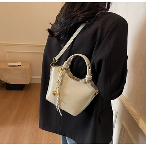 Detail of cream bucket bag with silk scarf charm and metal sphere on a model's shoulder