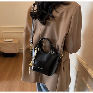 Detail of black glossy leather bucket bag with gold hardware and decorative scarf