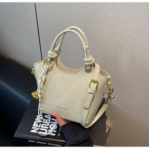 Detail of cream bucket bag with gold hardware and removable shoulder strap on book