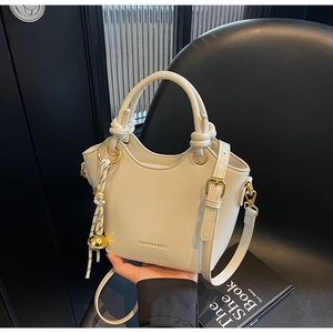 Close-up of beige minimalist bucket bag with gold ball charm on a modern black chair
