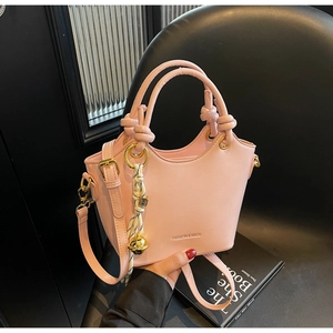 Pink minimalist bucket bag with long strap and striped bell charm on black background