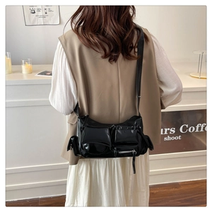 Detail of black glossy faux leather crossbody bag with multiple pockets and silver zippers