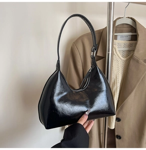 Detail of a sleek black glossy crescent handbag with smooth leather and a metal zipper