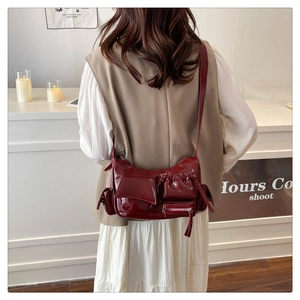 Detail of a dark red glossy leather crossbody bag featuring unique multi-functional pockets