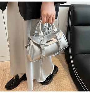 Detail of silver metallic handbag with pleated texture and silver buckles on sofa