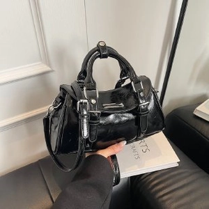 Detail view of a black patent leather handbag with silver hardware and detachable strap