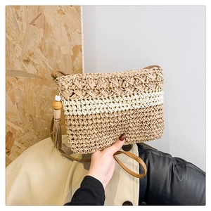 Detail of straw woven tote bag featuring bicolor texture and brown leather strap with tassel