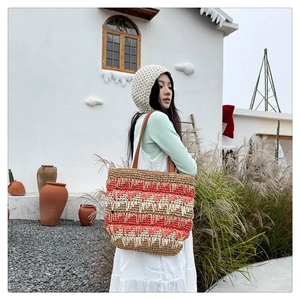 Detail of handwoven straw tote with orange and beige wave patterns and leather strap
