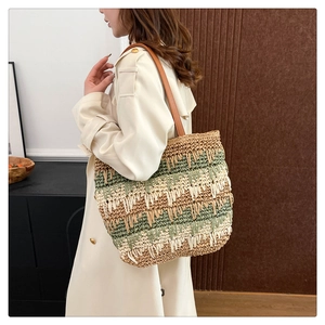 Detail of striped straw tote bag featuring woven texture and brown leather strap on model