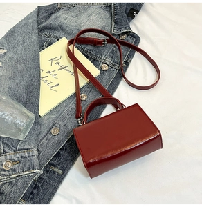 Détail d'un sac à main bordeaux brillant avec boucles argentées sur des jeans