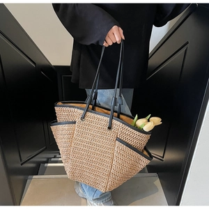 Dettaglio della grande borsa tote in paglia intrecciata con manici neri e fiori