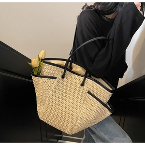 Dettaglio di una grande borsa tote in paglia con bordi in pelle nera e spalline sottili