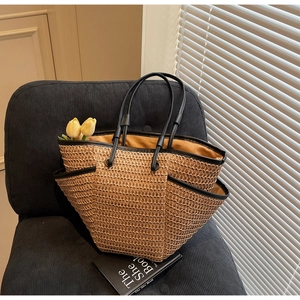 Dettaglio della borsa tote in paglia intrecciata con bordi neri e fodera gialla su poltrona