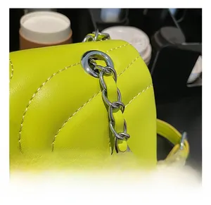 Macro shot of neon yellow crossbody bag featuring silver chain hardware and wavy stitching