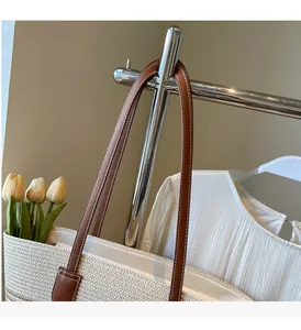 Detail of hand-woven straw tote bag with brown leather handles and decorative white stitching