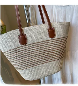 Detail of hand-woven striped straw tote bag featuring brown leather shoulder straps