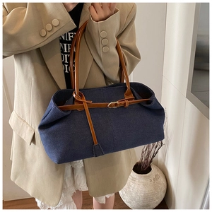 Détail d'un sac cabas en denim avec poignées en cuir marron et boucle décorative
