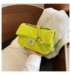 Detail of neon quilted shoulder bag with silver chain and twist lock on a wooden chair
