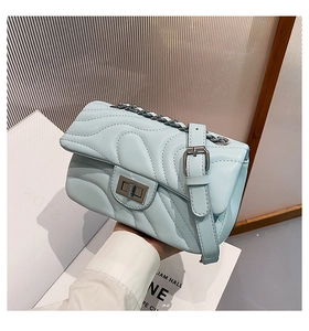 Detail of light blue quilted crossbody bag with metal twist lock and chain strap