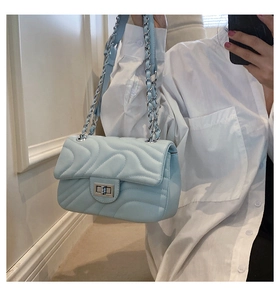 Detail of light blue quilted crossbody bag with silver chain strap and metal clasp