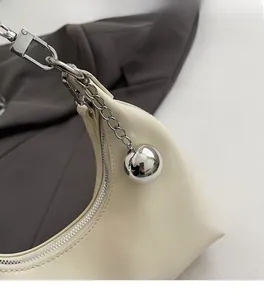 Détail du sac à bandoulière en cuir crème avec pendentif boule argentée et zip métallique