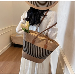 Straw tote bag with black stripes and leather handles shown on a model for travel