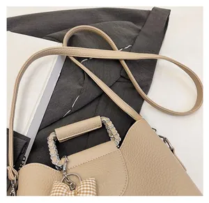 Detail of beige litchi grain leather bag with silver chain handle and bow charm