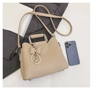 Detailed view of beige pebble leather handbag with pearl charm and metal feet protectors