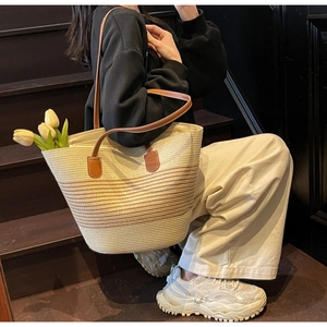 Detail of hand-woven straw tote bag featuring striped design and brown leather handles