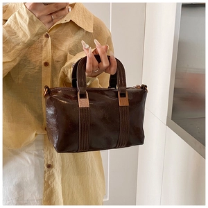 Detail of vintage dark brown handbag with stitching and golden hardware held by model