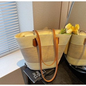 Detail of striped straw tote bag featuring brown leather handles and natural woven texture