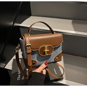 Detail of vintage denim and brown leather crossbody bag with gold oval twist lock closure