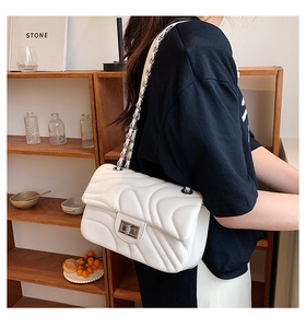 Detail of white quilted handbag featuring wave stitching and silver chain strap