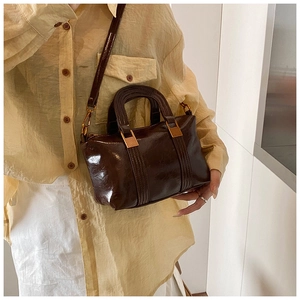 Detail of dark brown patent leather handbag with gold hardware and vintage stitching